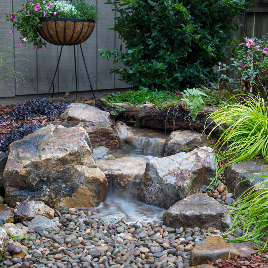 Small natural rock garden with a water feature, plants, and flowers.