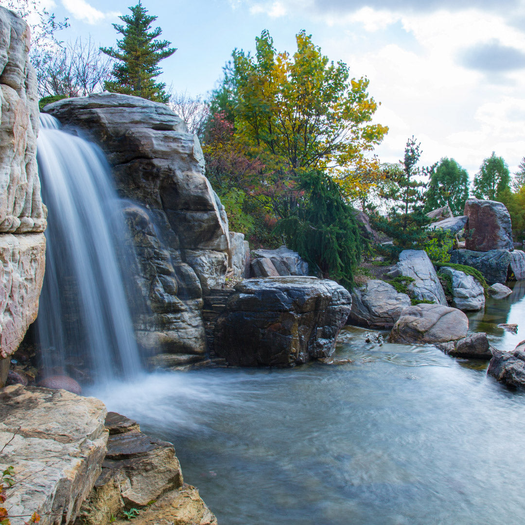 Waterfall cascading down rocky cliffs into a pool with trees and rocks in the background